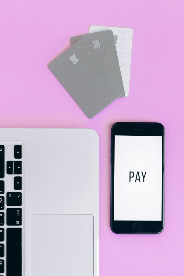 Vue de dessus d’une configuration de paiement mobile avec smartphone, cartes bancaires et ordinateur portable sur fond rose.